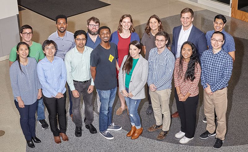 A group of people standing together indoors in a building lobby, posing for a group photo on a patterned floor.